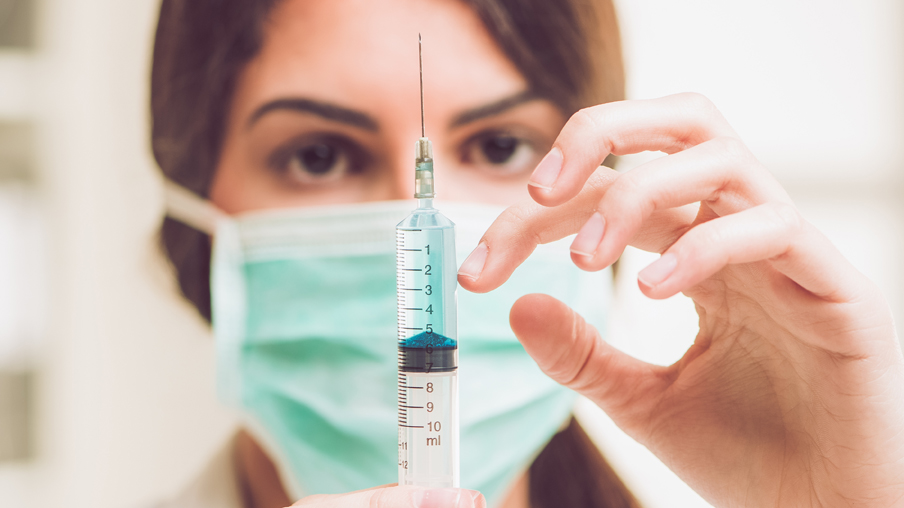 Enfermera con mascarilla manipula una jeringuilla